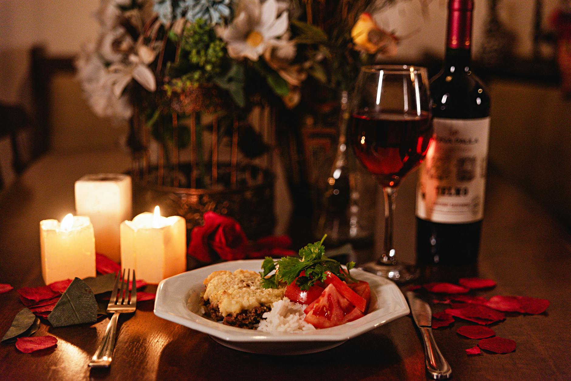 Cozy candlelit dinner with wine, gourmet meal, and rose petals