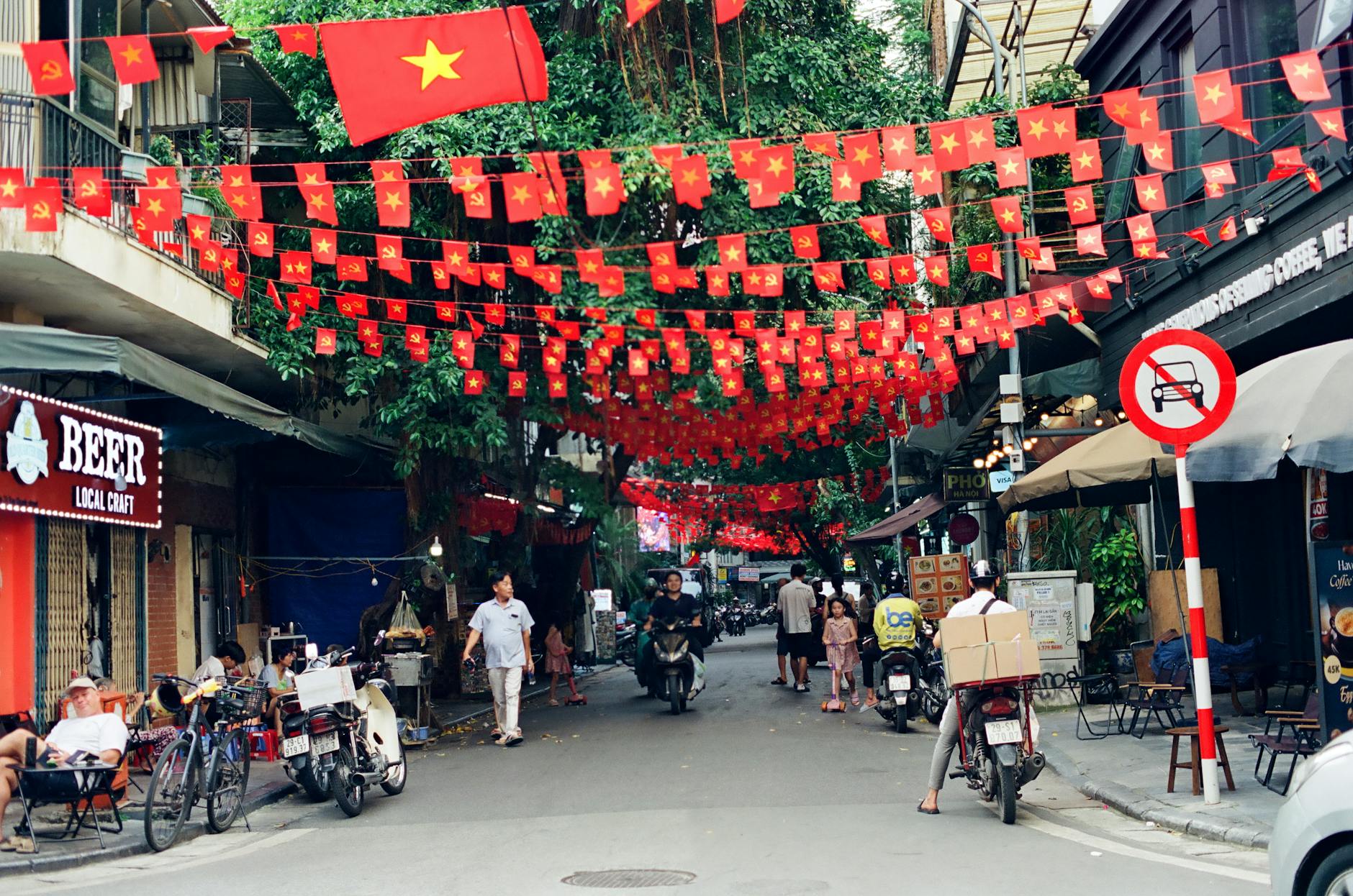 First Time Visiting Hanoi: Complete First-Timer's Guide (2026) 3 Vibrant Hanoi Old Quarter street with Vietnamese flags and motorbike traffic
