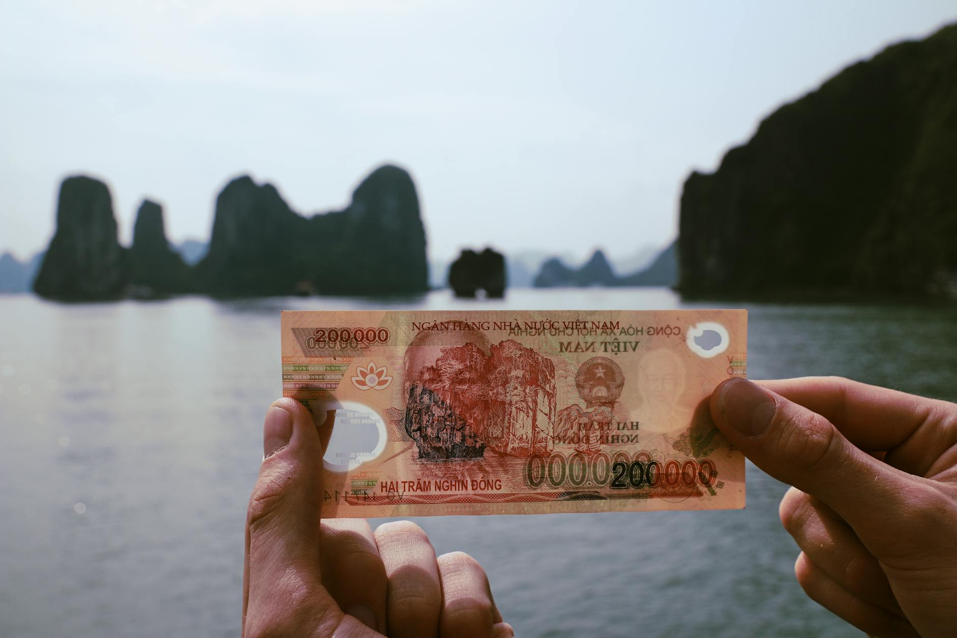 Hands holding Vietnamese Dong with Halong Bay scenery in background