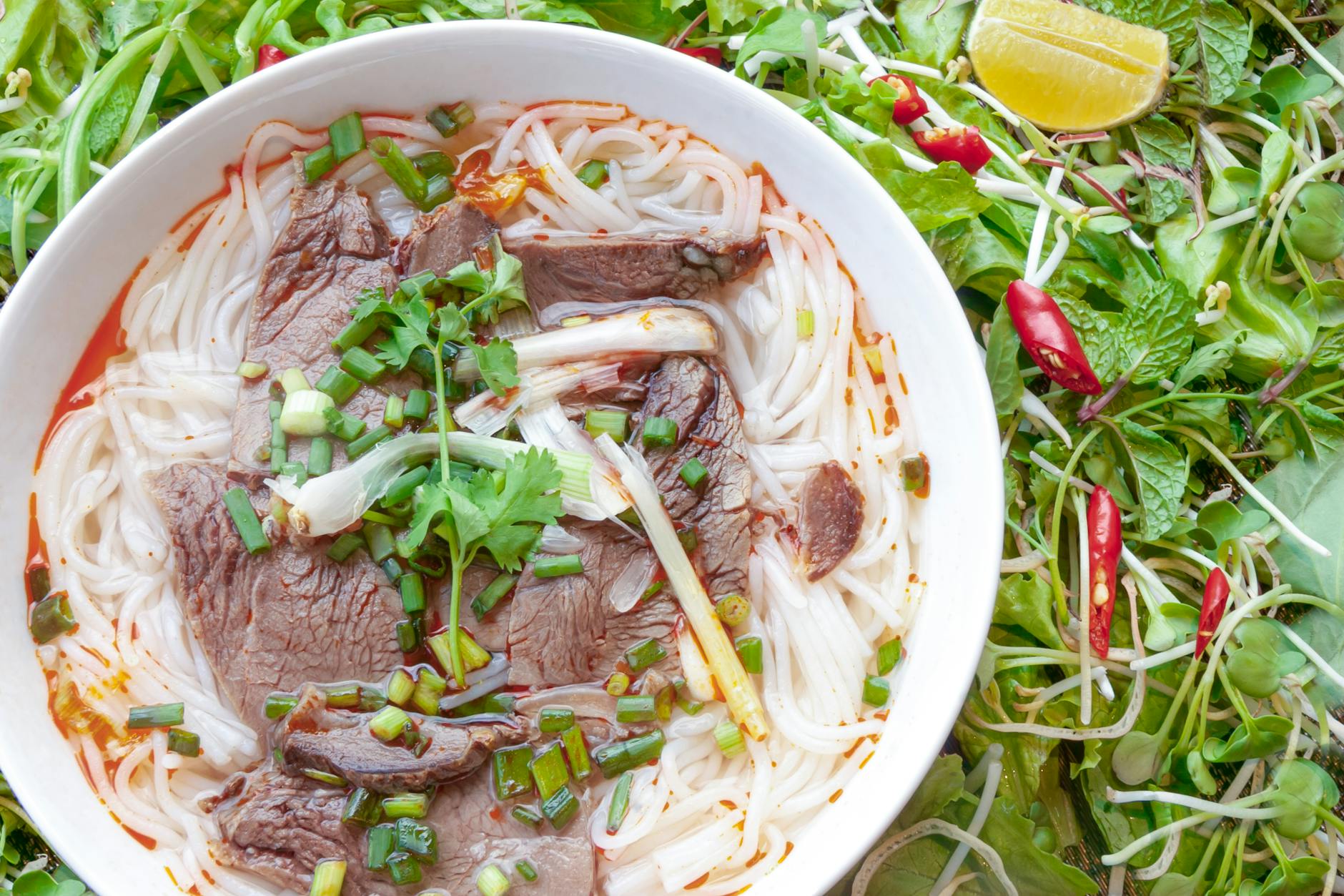 First Time Visiting Hanoi: Complete First-Timer's Guide (2026) 5 Steaming bowl of beef pho with fresh herbs and noodles served in Hanoi