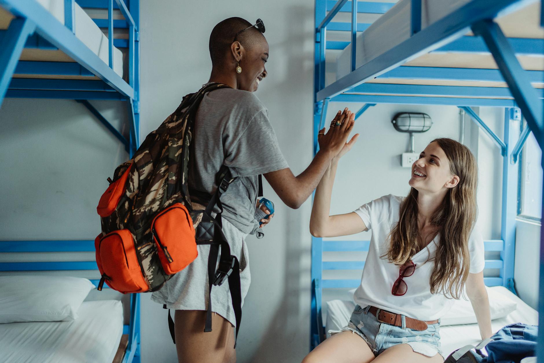 Hanoi for Solo Travelers: Complete Safety, Hostel & Activity Guide (2026) 3 Two female backpackers high-fiving in a bright hostel dorm room