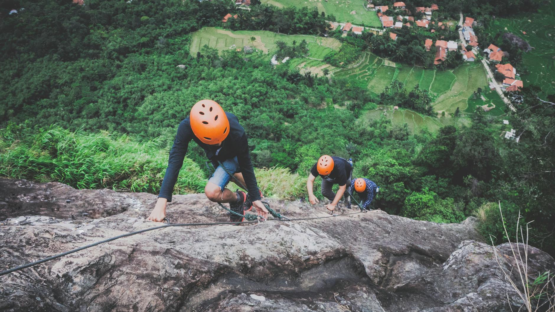 Three climbers ascending a rocky cliff with rice fields
