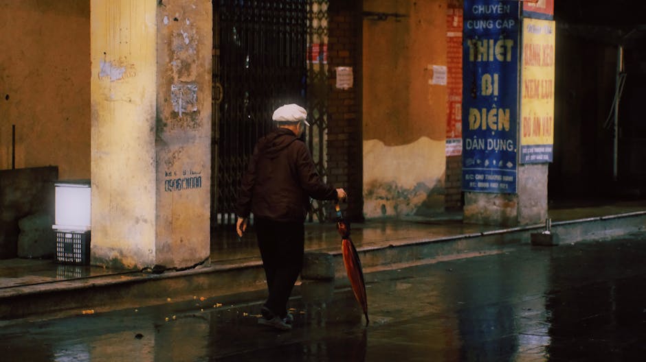 Hanoi in Summer: Heat & Rainy Season Travel Guide (2026) 3 Elderly man with umbrella on wet Hanoi street