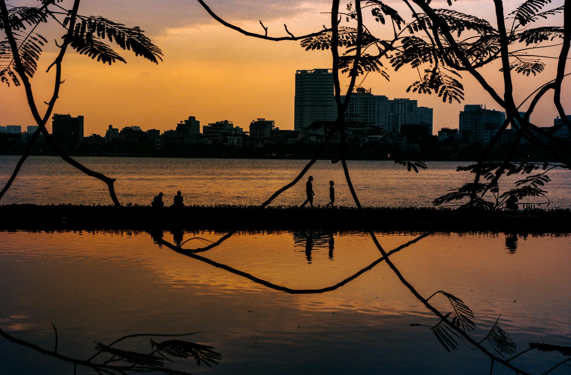 Silhouettes walking by West Lake at sunset in Hanoi