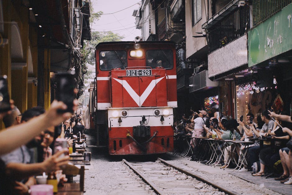 Red train moves through narrow Hanoi street with people watching